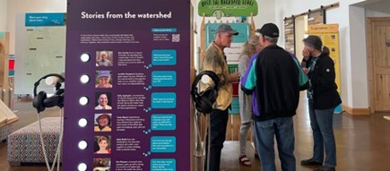 People in the We are Water MN exhibit with an interpretive sign with stories from the watershed