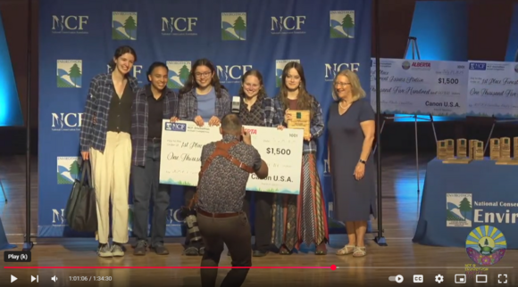 Winning team of 5 smiling on stage with a $1,500 scholarship check