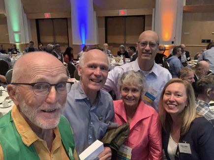 Cmsr. Edelson poses for a selfie with constituents at the Fresh Energy breakfast in a large conference room with people behind them.