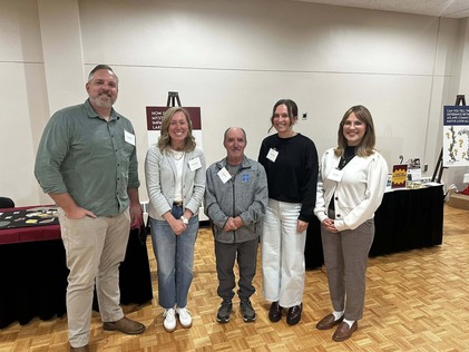 Cmsr. Edelson poses with Hennepin County staff and her two office staff in front of a presentation at the AIS forum; all are smiling.