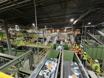 A photo of sorters at the Waste Management Recycling Facility; it shows many walkways, railings, and waste on conveyor belts.