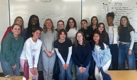 Heather poses, smiling, in a classroom at Edina High School, with about a dozen female students, also smiling.