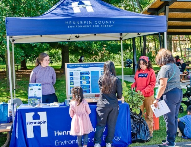 Hennepin staff work at a blue tent and speak with passersby about aquatic invasive species.