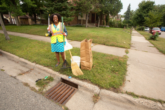 Person smiling holding supplies to clean out a storm drain while standing in front of a drain