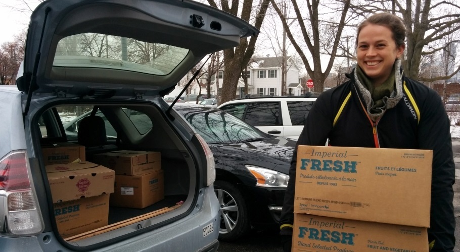 Woman standing by open trunk of car holding boxes of rescued produce