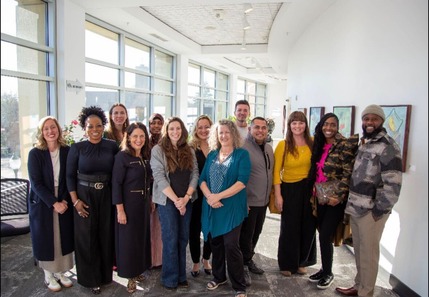 Commissioner Edelson stands on the far left side with CEO Now graduates in an area with windows. All are smiling.