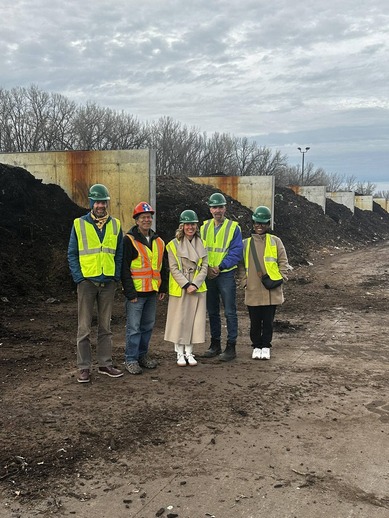 Commissioner Edelson poses with Commissioner Conley and other staffers, wearing hart hats, near compost bins.