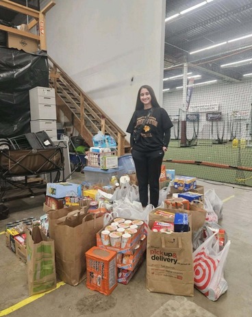 Edina High School student Mia Kapoor stands, smiling, in the middle of bags of the food she collected for her food drive.