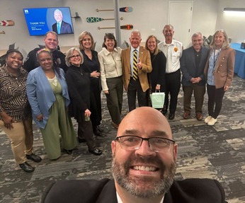 Minnetonka City Manager takes a selfie of the City Council meeting participants, smiling. Councilmembers and Edelson pose with Wiersum.