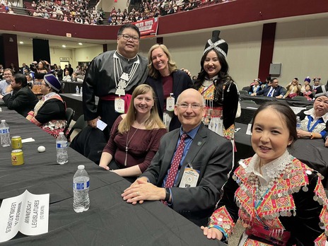 Heather poses with lawmakers and residents in a large room celebrating Hmong New Year.
