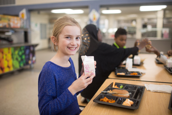 Group of students sitting at a school lunch table with food on reusable trays