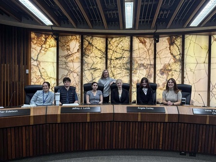 Heather smiles at the dais with interns sitting in front of her, all smiling.
