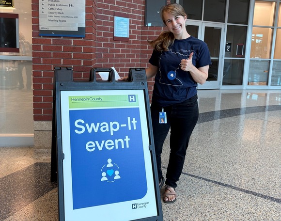 Hennepin County staff person smiling and giving a thumbs up by a swap-it sign
