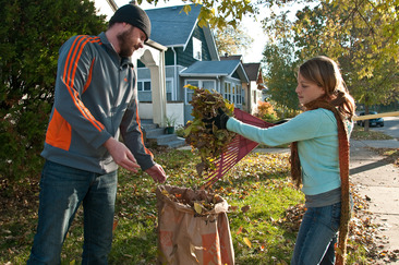 A man and woman clean up leaves by putting them in a bag on a sunny street in Hennepin County.