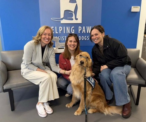 Heather and two staffers pose with a golden retriever in the middle of them, all smiling, in the lobby of Helping Paws.