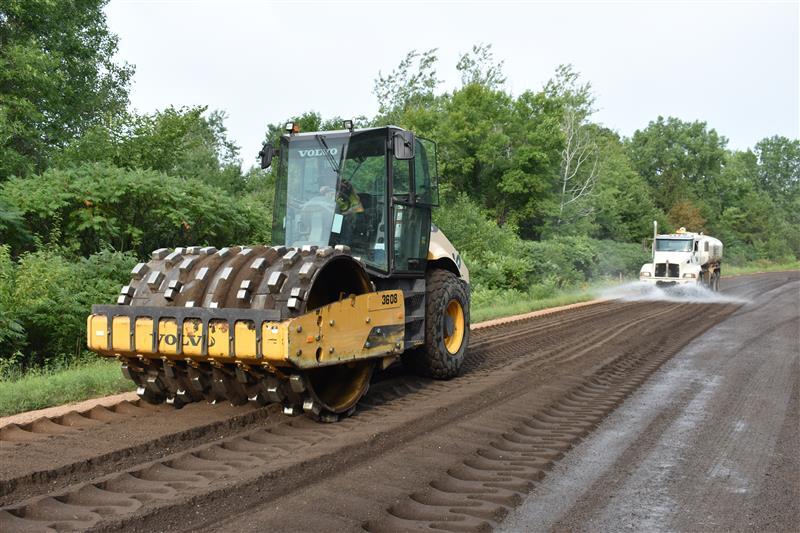 A bulldozer drives towards the camera, driving over a brown dirt road