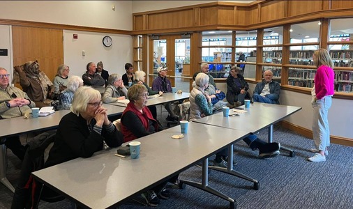A room of about 15 constituents speaks to commissioner Edelson as she listens in front of them in a room at the Hopkins library.