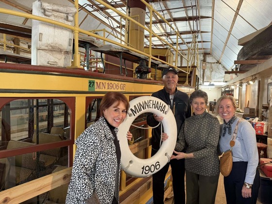 Heather smiles next to two community members in front of the steamboat in a warehouse.