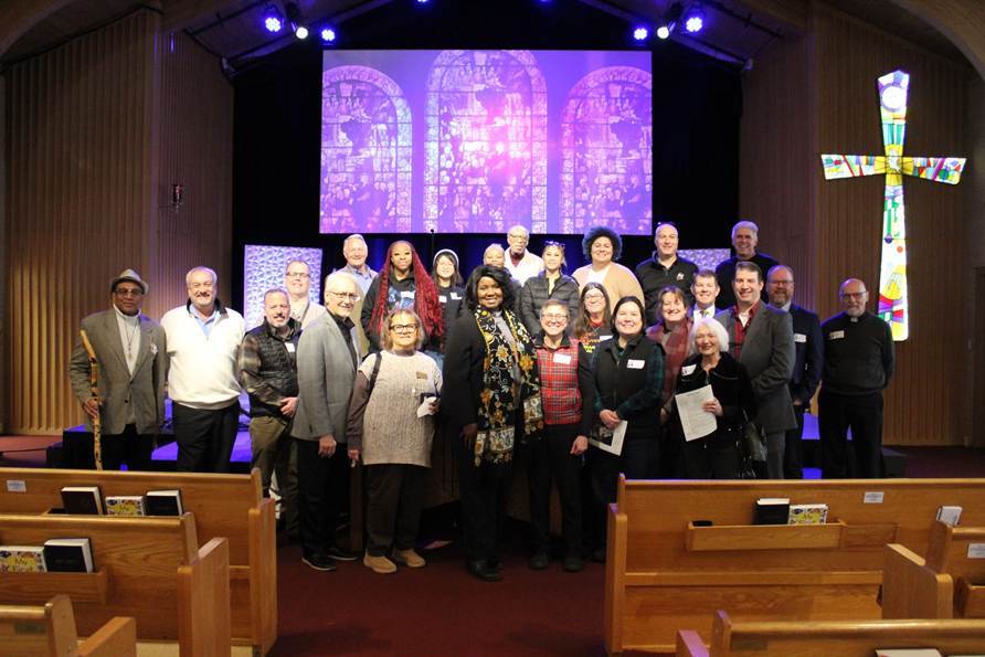 Group posing for photo at front of sanctuary; stained glass in background, pews in foreground