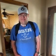 Smiling man wearing hat, glasses, and a backpack