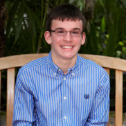 Smiling man wearing blue shirt and glasses sitting on a bench