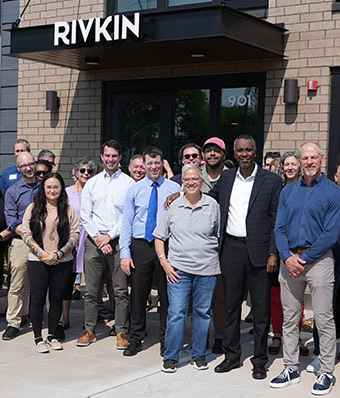 Close crop of people gathered in front of an apartment building entrance, named Rivkin