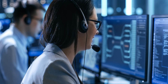 Woman wearing headset, smiling, facing her computer monitor in a call center.