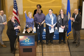 MNIT Central’s Quality Assurance Team receiving their award on stage and smiling, one giving a thumb’s up. Others on stage are applauding.
