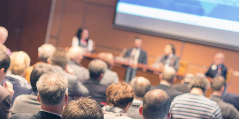 A panel of presenters speaking to a large group