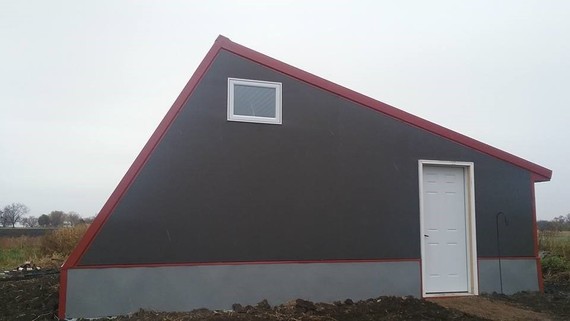 Side of a Deep Winter Greenhouse. Gray solid building with white door and small window at the top by the roof.