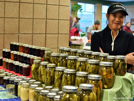 Employee behind the Schyma's Pickles & preserve vendor stand at Maple Grove indoor winter market