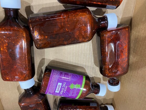Several bottles of Wonky Weeds-brand delta 9 THC syrup, with visible mold growth. One is labeled "Grape" flavor.