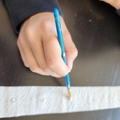 A hand holding a paint brush apply glue to create seed tape.