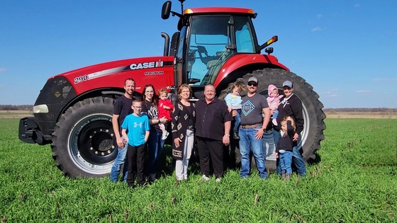 A family standing in front of a tractor in a field.