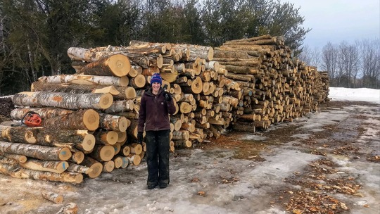 A farmer with a sledgehammer stands in front of a huge stack of lumber.