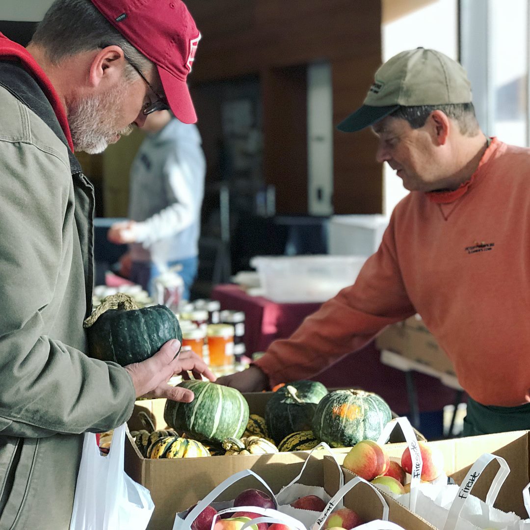 A farmers' market vendor and customer with winter squash.