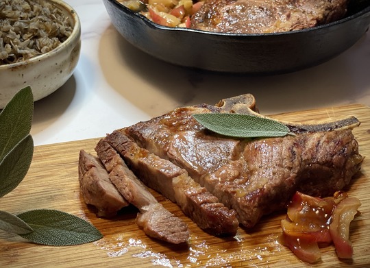 A sliced pork chop served with baked apples and wild rice.