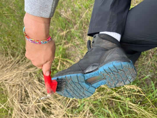A close-up of dirt being removed from a hiking boot with a handheld brush. 