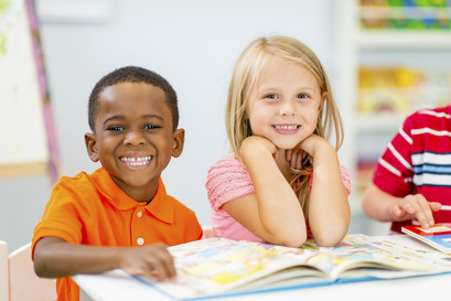 African American and Caucasian girl sit next to each other at a school table, smiling