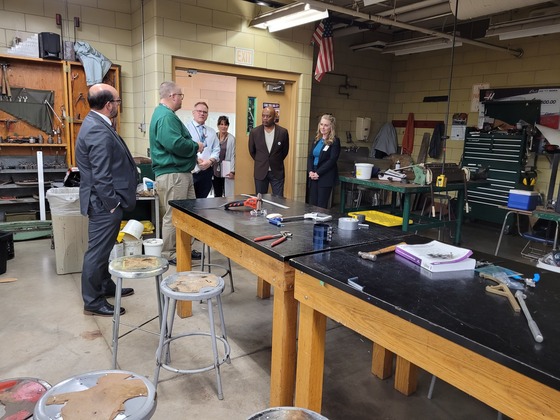 A teacher speaks to Commissioner Jett and two other men and two women in the doorway of a shop classroom