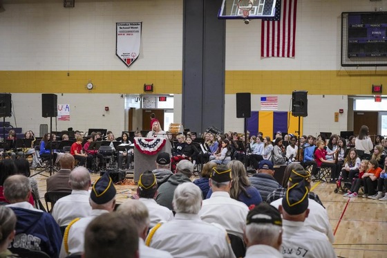 Chaska Middle School West Principal Alicia Fischer speaks at a podium in front of a large crowd including many veterans