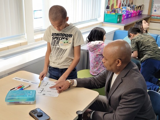 Commissioner Jett kneels down to work with a child on a computer science activity