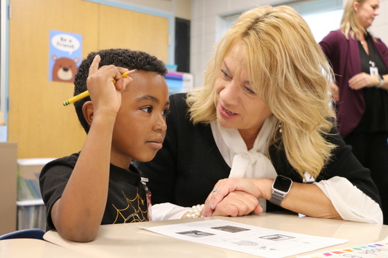 Julie Novak speaks to a young student working at his desk