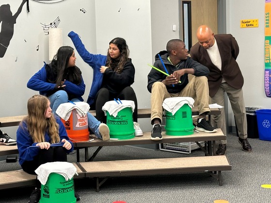 Commissioner Jett speaks with a student as students are practicing drumming on buckets during a music lesson