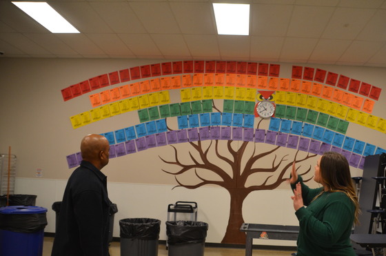 A woman talks with Commissioner Jett before a large mural featuring many different colors of paper