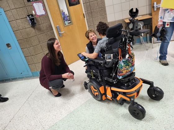 Stephanie Graff and another woman speak to a student using a wheelchair in a hallway