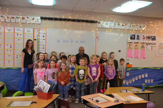 Commissioner Jett stands with students and a teacher in front of a white board that says “we drive for six miles” 