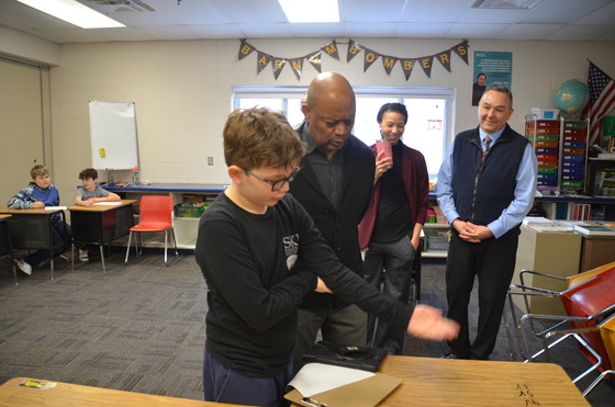 A student points to number sand letters on a desk as Commissioner Jett looks on