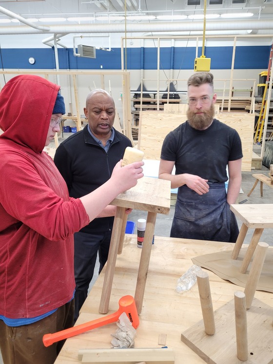 A student is using wood glue on a bench he is making as Commissioner Jett looks on