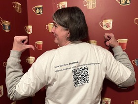 Jennifer Dugan wearing a T shirt with a QR code link to the MCA/Alternate MCA Review Committee signup